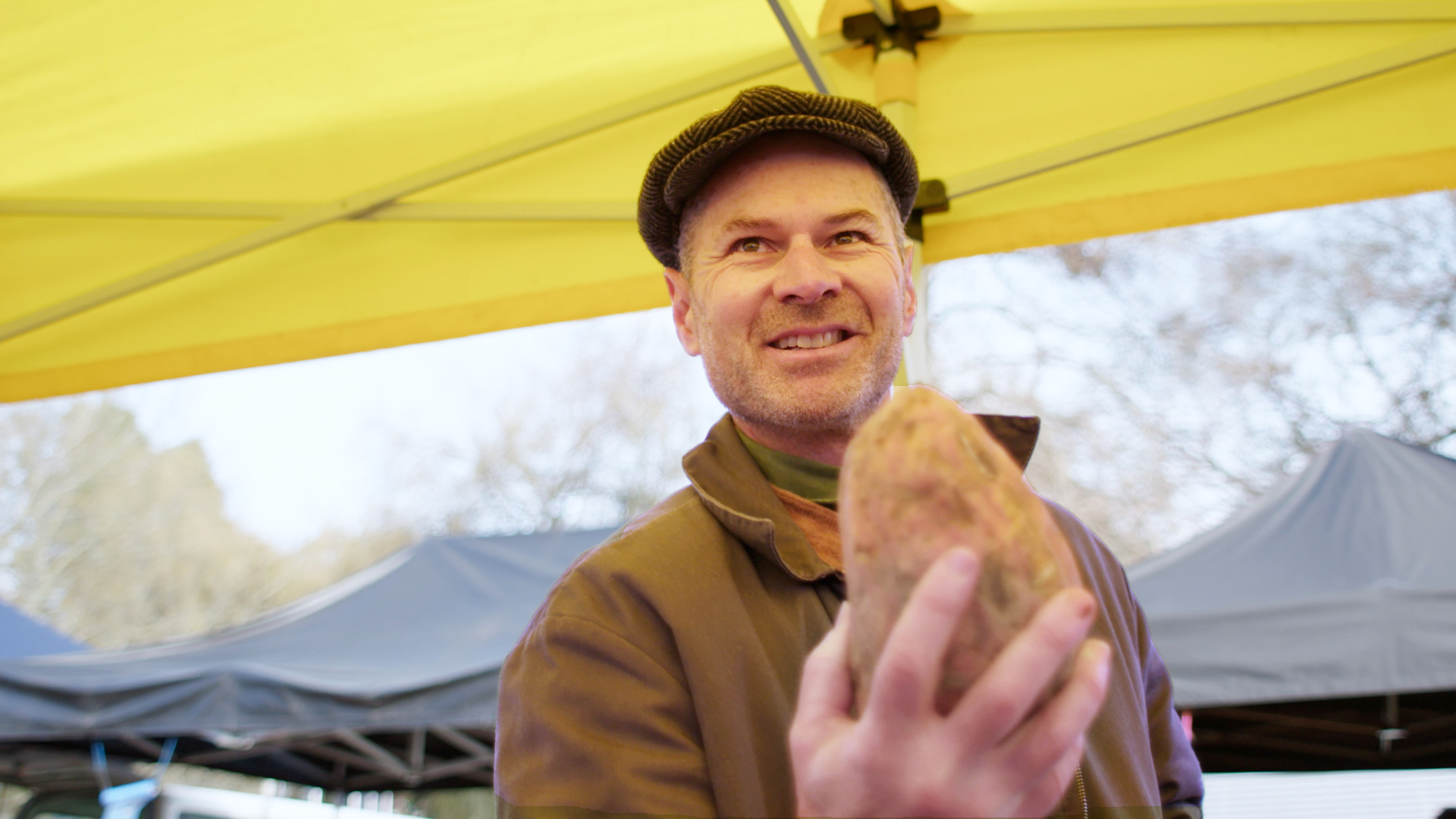 Toa Fraser holding a kumara at a market